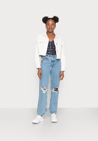 Jaqueta de ganga branca cortada, top de flores azul-marinho, jeans largas de ganga azuis claros com rasgos e ténis brancos. Design simples, ajuste casual e texturas suaves.
