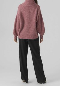 Übergroßer rosa Strickpullover mit hohem Kragen, strukturierter Stoff und langen Ärmeln, kombiniert mit schwarzen Cargohosen mit Seitentaschen.