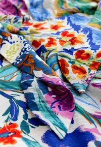 Stoff mit lebhaftem Blumendruck in Blau-, Rot-, Violett-, Grün- und Orangetönen, der gefaltete und überlappende Abschnitte zeigt.