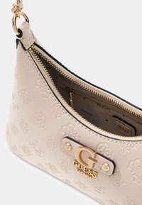 Beżowa skórzana torba na ramię z tłoczonym wzorem logo, złotymi elementami, zamkiem błyskawicznym i wewnętrzną kieszenią. Złote logo na przodzie.