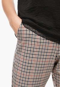 Rutiga byxor i beige, svart och rostfärg. Har en strukturerad midja och sidfickor. Svart topp med spetsdetalj i fållen.