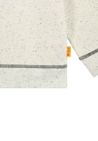 Hellgraues Sweatshirt mit Struktur und schwarzen Sprenkeln, mit einem gelben Etikett an der Naht und kontrastierenden schwarzen Nähten an Bündchen und Saum.