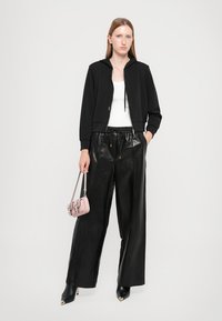 Svart avkortet hettegenser, hvit tank topp, blanke svarte vide lærbukser, og en liten rosa håndveske. Sleek svarte hæler fullfører antrekket.