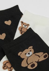 Schwarz-weiße Knöchelsocken mit braunen Teddybären und Herzmustern auf einem schlichten Hintergrund.