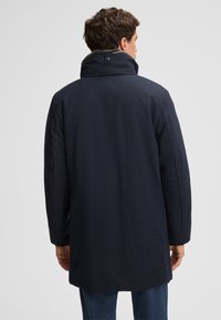 Cappotto blu navy con colletto alto e chiusura a bottoni, caratterizzato da una texture liscia e una vestibilità su misura, visto da dietro.