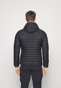 Veste rembourrée noire avec capuche, présentant un design matelassé, une texture lisse et des poignets élastiques. La vue arrière montre une coupe ajustée et un matériau léger.