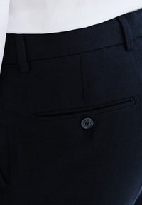 Granatowe spodnie z teksturowanej tkaniny, z tylną kieszonką zapinaną na guzik oraz płaskim przodem.