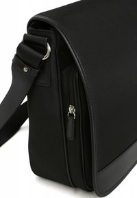 Zwarte messenger bag met textuur, een soepele leren bodem, een ritscompartiment en een verstelbare strap met zilverkleurige hardware.