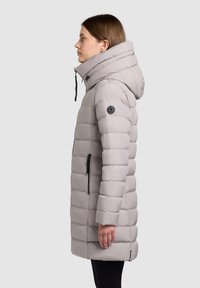 Grey padded winter coat with a high collar, hood, side zipper pocket, and textured quilted design; features black logo accent.