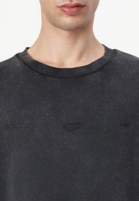 Dark gray sweatshirt with a ribbed crew neck. Features a subtle logo and text embroidered on the chest. Soft, textured fabric.