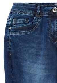 Jeans en denim bleu foncé avec poche avant, petite poche à monnaie, passants de ceinture et fermeture par bouton métallique sur fond blanc.