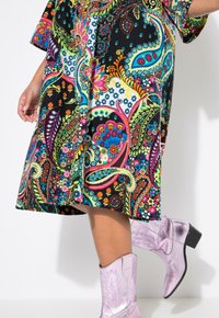 Vestido de longitud a la rodilla colorido con un patrón de paisley en tonos de azul, rosa y verde sobre un fondo negro, combinado con botas brillantes de color lavanda.