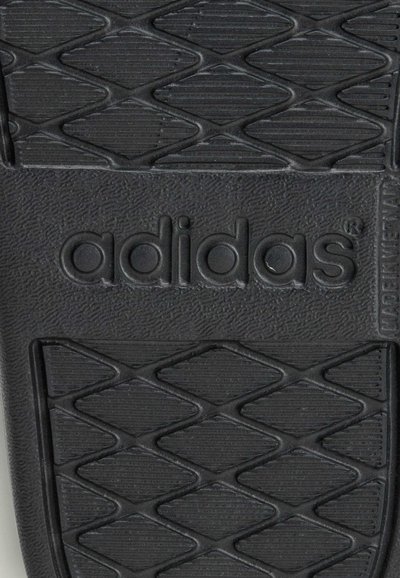 Semelle de sandale en caoutchouc noir avec surface texturée, présentant un motif en losanges et le nom de la marque "adidas" en relief, bien visible.
