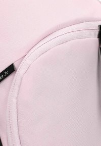 Tissu rose texturé avec une finition lisse, présentant un design arrondi et une étiquette noire. Des détails de couture sont visibles le long des bords.
