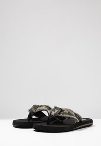 Flip-flop con suole in gomma nera e una cinturino in tessuto mimetico con bordi sfilacciati. Design semplice adatto per un uso casual.