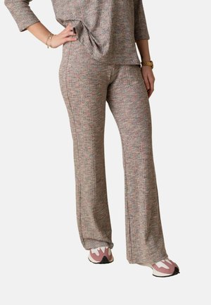 Mujer vestida con un top de punto texturizado de manga larga a juego y pantalones acampanados con zapatillas rosas y blancas, mano apoyada en la cadera.