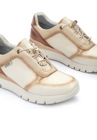 Zapatos de cordones en beige y marrón claro con un acabado de cuero suave y paneles laterales texturizados. Suelas elevadas y acolchadas, con detalles metálicos.