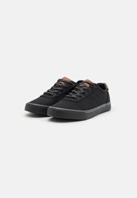 Svarta canvas-sneakers med texturerade svarta gummisulor, som har bruna läderdetaljer på tungan och klacken, samt svarta snören.