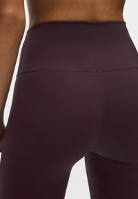 Högmidjade leggings i djupt burgundröd, tillverkade av ett mjukt, elastiskt material. Har platta sömmar och en skräddarsydd passform för komfort.