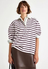 Overdimensjonert hvit poloskjorte med mørkelilla striper, med krage og oppbrettede ermer. Mykt bomullsmateriale.