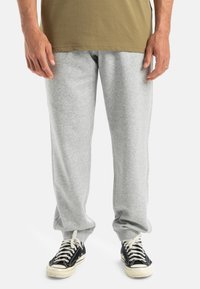 Grisierte Sweatpants aus weichem Stoff mit lockerer Passform und elastischen Bündchen, kombiniert mit schwarzen Sneakers mit weißen Sohlen und Schnürsenkeln.