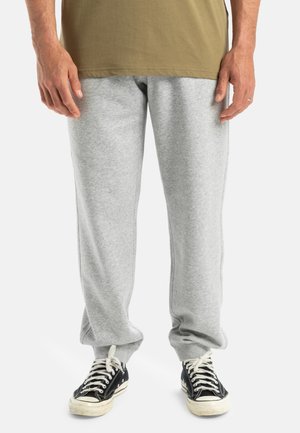 Grijze sweatpants gemaakt van zacht materiaal, met een relaxte pasvorm en elastische boorden, gecombineerd met zwarte sneakers met witte zolen en veters.