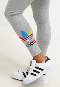 Grå leggings med flerfärgad Adidas-logga och ränder i blått, gult och rött. Kombineras med svart-vita Adidas Superstar-sneakers.