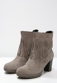 Bottes chevilles en daim gris avec des franges verticales, un bout rond et un talon empilé. Présente des coutures contrastantes le long de la semelle.
