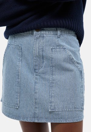 Gros plan sur une jupe à rayures verticales bleu et blanc avec des poches plaquées à l'avant, portée avec un pull bleu marine foncé.