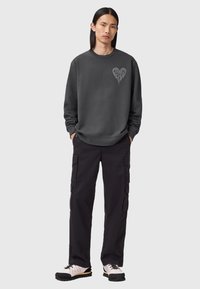 Mørkegrå sweatshirt med et grafisk hjerte-design, parret med sorte cargo-bukser og lyse sko, der skaber et afslappet outfit.