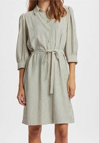 Vestito a scacchi in crema e nero, con chiusura frontale a bottoni, vita legata e maniche a palloncino. Realizzato in tessuto leggero con una vestibilità comoda.