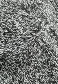 Pleteni tekstil u crno-bijeloj boji s debelom, masivnom teksturom. Pređa sadrži mješavinu uvijenih vlakana koja stvaraju uzorčenu površinu.