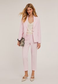 Completo su misura di colore rosa chiaro con giacca a un bottone, pantaloni cropped coordinati e un top in maglia crema. Accentuato da una borsa con stampa serpente.