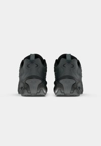 Egy fekete sportcipő pár hátulról, texturált talppal és húzófülekkel, fehér háttér előtt.