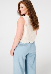 Crop top en dentelle florale couleur crème avec ourlet festonné, associé à un jean bleu clair à jambes larges avec une poche arrière.