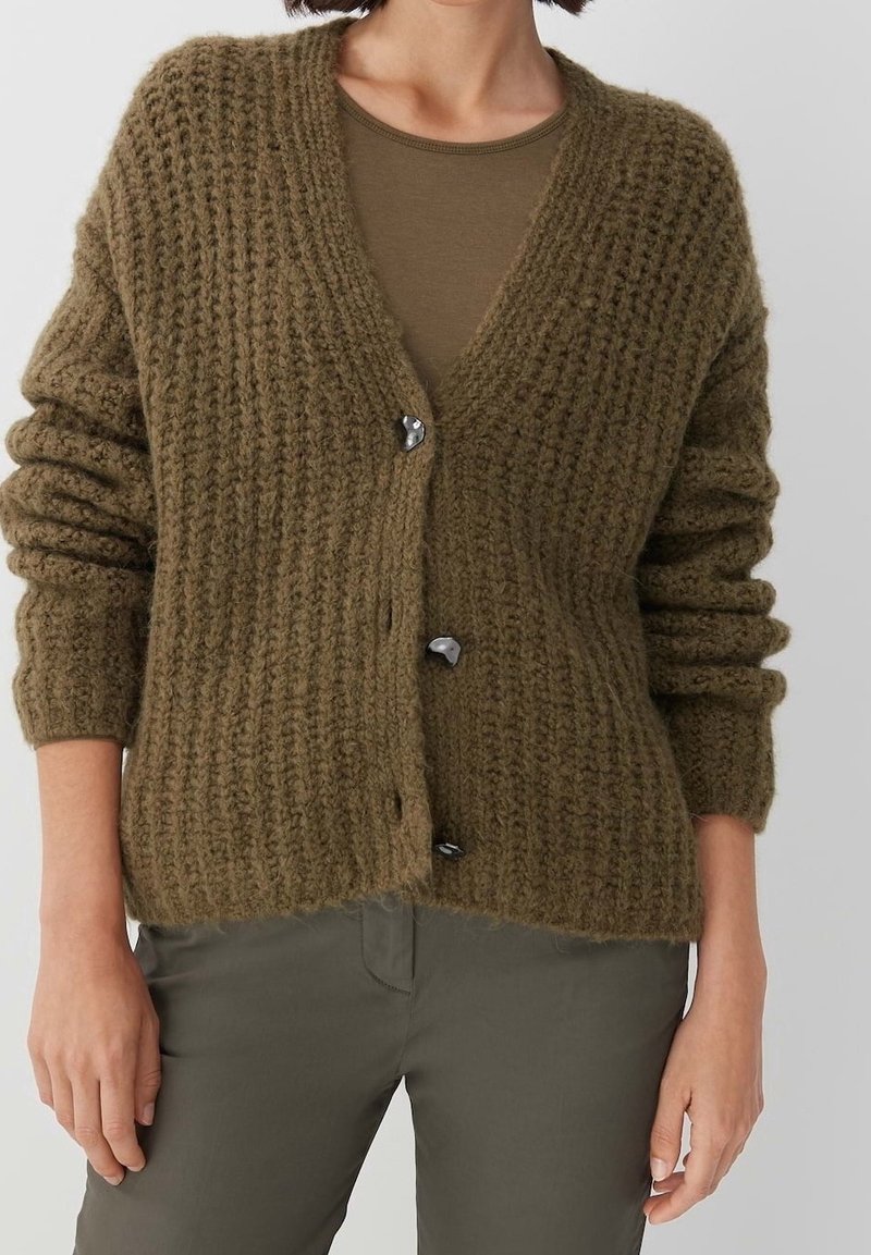 Olivgrön stickad cardigan med kraftig textur, djup V-ringning och tre svarta knappar fram. Långa, lätt puffade ärmar.