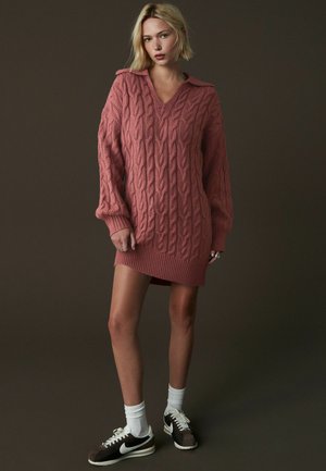 Cable-knit klänning i dammig rosa med V-ringning, långa ärmar och ribbad nederkant. Matchad med mörka sneakers och vita strumpor.