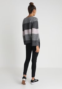 Grau gestreifter Pullover mit hellrosa Akzenten, gestrickter Textur, weiten Ärmeln und lockerem Sitz, kombiniert mit schwarzen Skinny-Jeans und Turnschuhen.