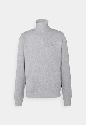 Pilkas zip-futbolo megztinis, minkšta medžiaga, ilgomis rankovėmis, su įriebalais raiščiais ir apykakle, su mažai žalia logotipu ant krūtinės.