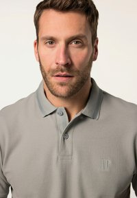 Polo gris con un acabado texturizado, dos botones en el cuello y un logotipo sutil bordado en el pecho. Cuello acentuado en un tono más claro.