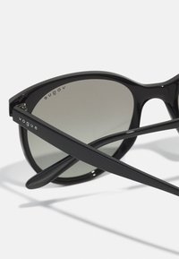 Ochelari de soare din plastic negru, cu un cadru curbat și lentile gri cu degradé. Se remarcă prin brandul "vogue" pe braț. Două brațe subțiri.