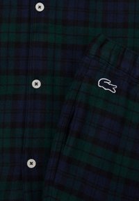 Πλαίσιο πουκάμισο σε σκούρο πράσινο και μπλε ναυτικό. Διαθέτει λευκά κουμπιά και ένα μικρό λευκό κεντημένο λογότυπο κροκοδείλου στην τσέπη. Μαλακή υφή υφάσματος.