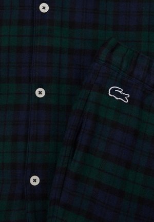 Koszula w kratę w ciemnozielonym i granatowym kolorze. Posiada białe guziki oraz małe, białe haftowane logo krokodyla na kieszeni. Miękka faktura materiału.