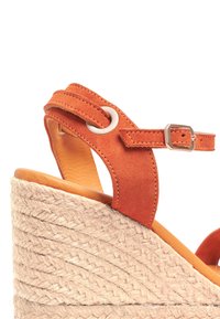 Sandale compensée en daim orange avec un talon en jute tressé, une sangle de cheville ajustable et une semelle intérieure en cuir lisse. Présente un accent en métal.