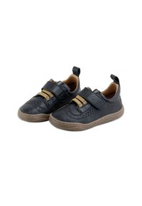 Zapatos de cuero negro con acentos en marrón, que cuentan con una correa de Velcro, suela marrón texturizada y costuras decorativas a lo largo de los bordes.