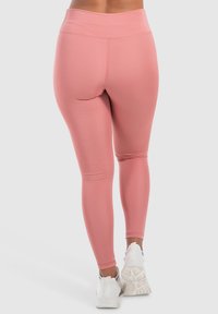 Leggings rosa con vita alta, texture liscia e design aderente, abbinati a scarpe da ginnastica bianche.