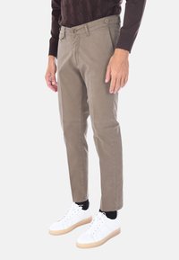 Pantaloni chinos color crema con vestibilità slim, due tasche frontali e una texture sottile, abbinati a scarpe da ginnastica bianche e calzini neri.