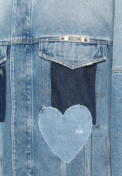 Světle modrá denimová bunda s tmavě modrými náplety, nášivka ve tvaru srdce a značka Moschino umístěná nad kapsou.