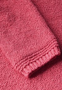 Texturerat rosa tyg vikt, med ett mjukt, stickat utseende och en ribbad kant. Ytan är varm och inbjudande med en mysig framtoning.