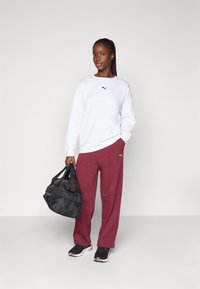 Pulover alb cu logo negru, pantaloni de trening burgundy, pantofi negri și o geantă de sport neagră cu mânere duble. Țesătură netedă, croială lejeră.